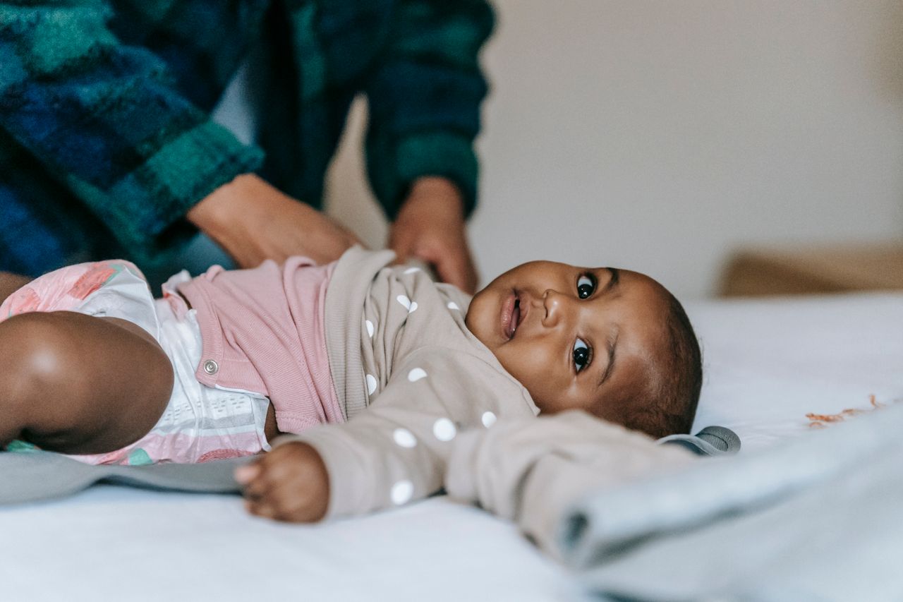 Adorable small African American infant in diaper lying on sheet near crop anonymous mother